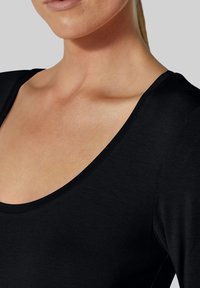 Schwarzes Top mit Rundhalsausschnitt und kurzen Ärmeln, aus glattem, leichtem Stoff gefertigt, der eine enge Passform bietet und das Dekolleté sowie die Schultern betont.