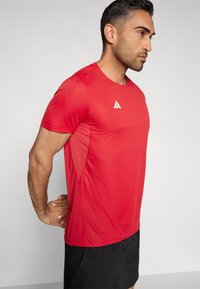 Punane kerge spordisärk, millel on lühikesed varrukad ja ümmargune kaelus ning valge logo rinnal.