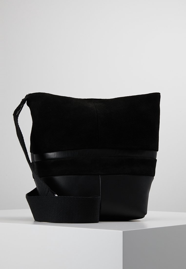 Czarna torebka z zamszowym wierzchem i skórzanym dnem, z szerokim paskiem i eleganckim, minimalistycznym designem.