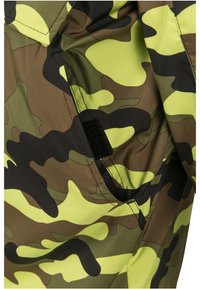 Kamouflage-tyg i nyanser av grönt och gult med en slät yta. Har ett kardborreband och ett distinkt abstrakt mönster.