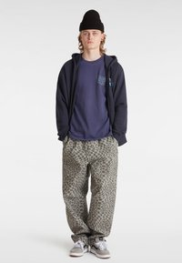 Marineblauer Hoodie über einem marineblauen T-Shirt mit Grafik, kombiniert mit grauen, gemusterten Hosen mit Leopardenmuster, abgerundet mit grauen Sneakers.