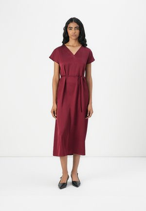 Burgundy midi dress with short sleeves, V-neck, and a waist belt. Smooth, shiny texture. Worn with black pointed-toe shoes.