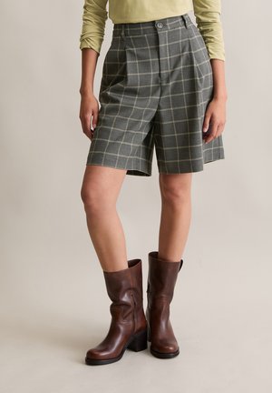 Grijze geruite shorts met plooien en een knoopsluiting, gecombineerd met bruine leren kniehoge laarzen met een blokhak.