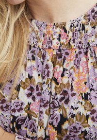 Bloemenpatroon jurk met een smockhalslijn. Kleuren zijn lavendel, roze en olijfgroen op een witte achtergrond van textuurstof.