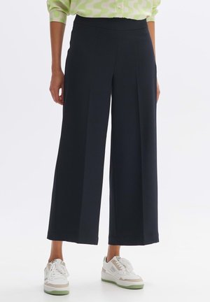 Wide-leg trousers in textured navy fabric with a smooth waistband, paired with white sneakers featuring light green accents.