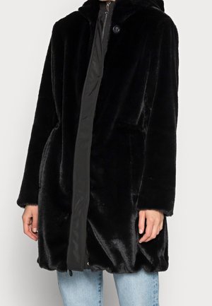 Czarny płaszcz z imitacji futra z kapturem, zapinany z przodu na zamek i guziki, noszony na jasnoniebieskich dżinsach, widoczny od połowy uda do szyi.