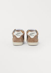 Baskets en suède marron avec une finition texturée, accents en cuir blanc, onglet au talon bleu et semelle contrastante beige. Marque visible sur le talon.