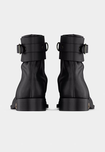Ζευγάρι μαύρα δερμάτινα μποτάκια αστραγάλου με χοντρές σόλες και ρυθμιζόμενα λουριά με αγκράφες στο πάνω μέρος, σε προβολή από πίσω.
