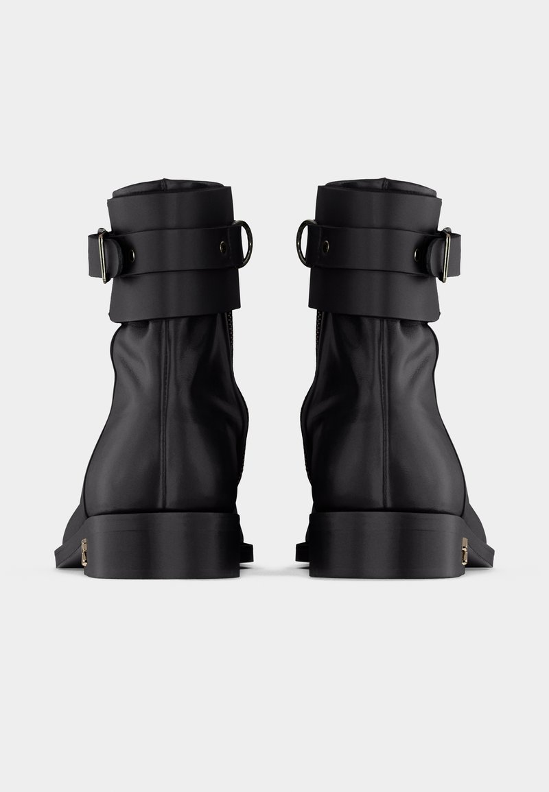Coppia di stivaletti alla caviglia in pelle nera con suole spesse e cinturini regolabili con fibbia nella parte superiore, visti da dietro.