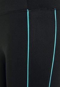 Černé legíny s hladkým povrchem mají kontrastní tyrkysové postranní švy. Design zahrnuje ploché švy pro zvýšení odolnosti.