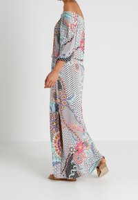 Sukienka maxi z dekoltem off-shoulder, kolorowymi wzorami kwiatowymi, czarno-białymi akcentami geometrycznymi oraz rozcięciem z boku. Lekka, zwiewna tkanina.