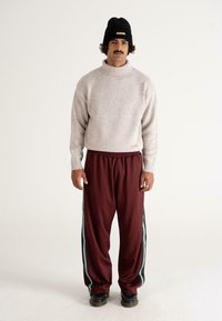 Strick-Turtleneck-Pullover in Hellgrau mit einem gesprenkelten Muster, kombiniert mit bordeauxfarbenen Jogginghosen mit grünen Seitestreifen und einem Kordelzug.