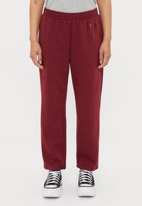 Pantaloni della tuta bordeaux con vita elastica, tasche laterali e una piccola striscia verticale a sinistra. Tessuto in misto cotone.