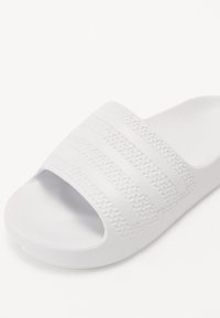 White slide sandal with an open-toe design, textured strap featuring three horizontal ridges, and a smooth, molded footbed.