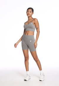 Szary sportowy crop top i szorty o wysokim stanie wykonane z teksturowanej tkaniny. Oba elementy mają małe logo. Obuwie to białe sneakersy.