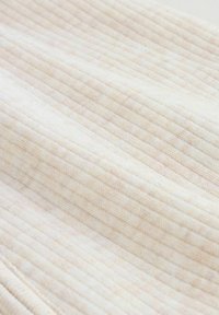 Close-up van een zachte, licht beige geribbelde gebreide stof met een fijn horizontaal patroon en textuurdetails.