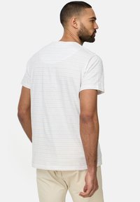 Weißes T-Shirt mit kurzen Ärmeln und dezenten horizontalen Streifen in Blau und Rot. Weicher Stoff mit Rundhalsausschnitt und lockerer Passform.