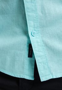 Lichtblauw linnen shirt met een gladde textuur, voorzien van een knoopsluiting en een genaaide label aan de zijkant. Casual pasvorm met een ronde zoom.