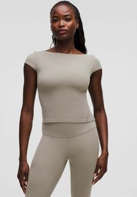 Beige aangesloten top met korte mouwen en een vierkante halslijn, gemaakt van rekbaar materiaal. Stikdetails langs de zijkanten en de zoom.