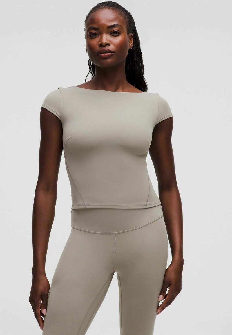 Beige aangesloten top met korte mouwen en een vierkante halslijn, gemaakt van rekbaar materiaal. Stikdetails langs de zijkanten en de zoom.