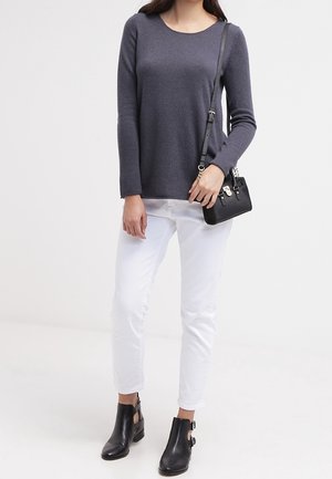 Maglione grigio a maniche lunghe con scollo a barca, pantaloni bianchi aderenti e stivaletti neri alla caviglia. Una piccola borsa a tracolla nera viene portata sulla spalla.