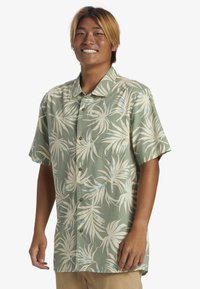 Camisa de botones de manga corta en verde claro, con un patrón de hojas de palma blancas y azules, con un bolsillo en el pecho y un corte relajado.