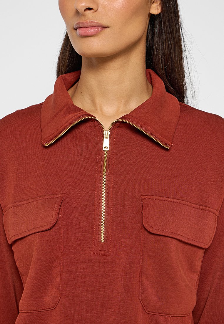 Roodbruine cardigan met rits en kraag, gouden rits en twee borstzakken. Gemaakt van textuurstof met een ontspannen pasvorm.