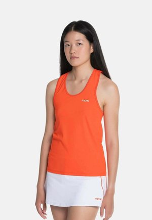 Junge Frau mit langen schwarzen Haaren, die ein oranges ärmelloses Oberteil und einen weißen Sportrock trägt, auf beiden ist das "nox"-Logo zu sehen.