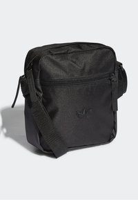 Černá crossbody taška vyrobená z texturovaného materiálu. Obsahuje zipovou přední kapsu, nastavitelný popruh a embosované logo na přední straně. Čtvercový tvar.