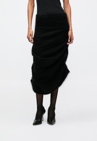 Saia preta, fofa, com um design drapeado, apresentando uma textura suave e uma bainha assimétrica. Usada com saltos altos pretos e collants.