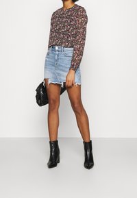 Långärmad blommig topp på en person som är kombinerad med en jeanskjol med fransar. Svarta ank stövlar och en strukturerad svart handväska kompletterar outfiten.