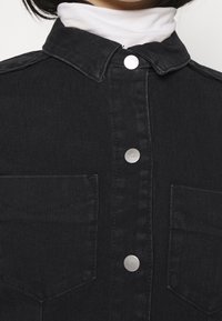 Černá denimová košile s špičatým límcem, stříbrnými patentkami a dvěma náprsními kapsami s hladkým povrchem.