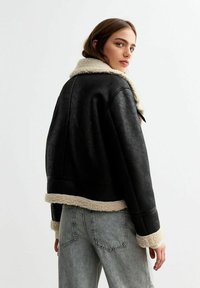 Giacca in finta pelle nera con colletto e orlo in shearling crema, design corto, maniche lunghe e superficie testurizzata.