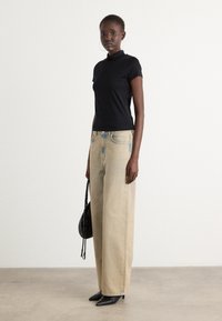Zwart T-shirt met korte mouwen, gecombineerd met lichtblauwe wijde jeans met versleten accenten. Zwarte hoge hakken en een kleine zwarte handtas.