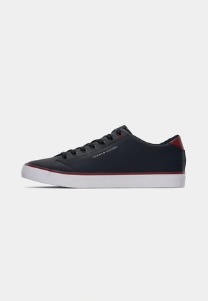 Niedrig geschnittener schwarzer Sneaker mit weißer Sohle, roten Akzenten, schwarzen Schnürsenkeln und Tommy Hilfiger Logo an der Seite, seitlich gezeigt.