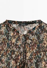 Blommönstrad genomskinlig blus med rund halsringning och knytning framtill, visar etiketten "Massimo Dutti Made in Morocco."
