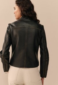 Zwarte leren jack met een slim fit ontwerp, voorzien van een hoge kraag en ritsmanchetten. Gladde textuur met zichtbare naden.