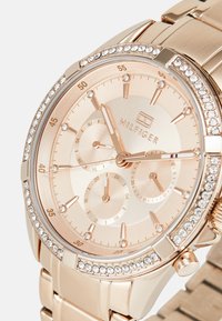 Montre en or rose avec un cadran rond, une lunette en cristal et trois sous-cadrans. Présente un bracelet en métal et des marqueurs d'heure gravés.
