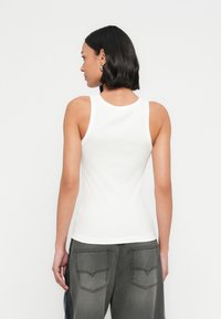 Λευκό ριμπ αμάνικο τοπ με στρογγυλή �λαιμόκοψη και χωρίς μανίκια, συνδυασμένο με σκούρα γκρι ψηλόμεσα παντελόνια που διαθέτουν διακοσμητικές τσέπες.