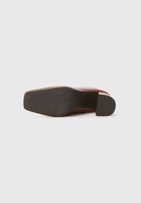 Zapato de cuero marrón con una suela de goma texturizada, tacón cuadrado y un acabado suave. Presenta mínimos elementos decorativos.