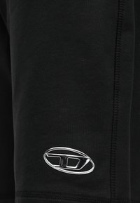 Κοντινή λήψη μαύρου υφάσματος με κάθετες ραφές και ένα μικρό ασημένιο οβάλ καρφίτσα κλειδώματος προσαρτημένη κοντά στο κάτω μέρος.