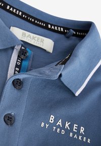 Plava polo majica napravljena od teksturiranog materijala, sa bijelim kragnom, crnim dugmadima i izvezenim logotipom "BAKER by TED BAKER."