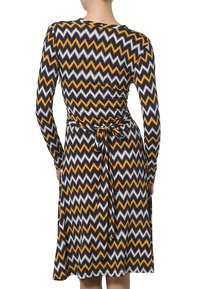 Vestido de manga larga con un patrón en zigzag en negro, blanco y naranja, con un detalle de cintura atada y una falda acampanada.