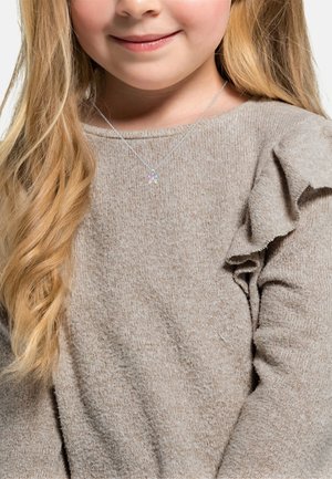 Hellbrauner Pullover mit Rüschendetails an den Schultern, kombiniert mit einer silbernen Halskette, die einen Schmetterlingsanhänger in Pastellfarben trägt.