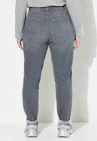 Pantalones de mezclilla grises con un corte cónico, que cuentan con dos bolsillos traseros, puños enrollados y una textura suave. Combinados con zapatillas deportivas plateadas.