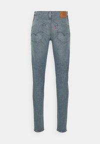 Jeans de mezclilla azul claro con piernas estrechas, que cuentan con dos bolsillos traseros y una etiqueta de cuero marrón en la cinturilla con detalle de costura.
