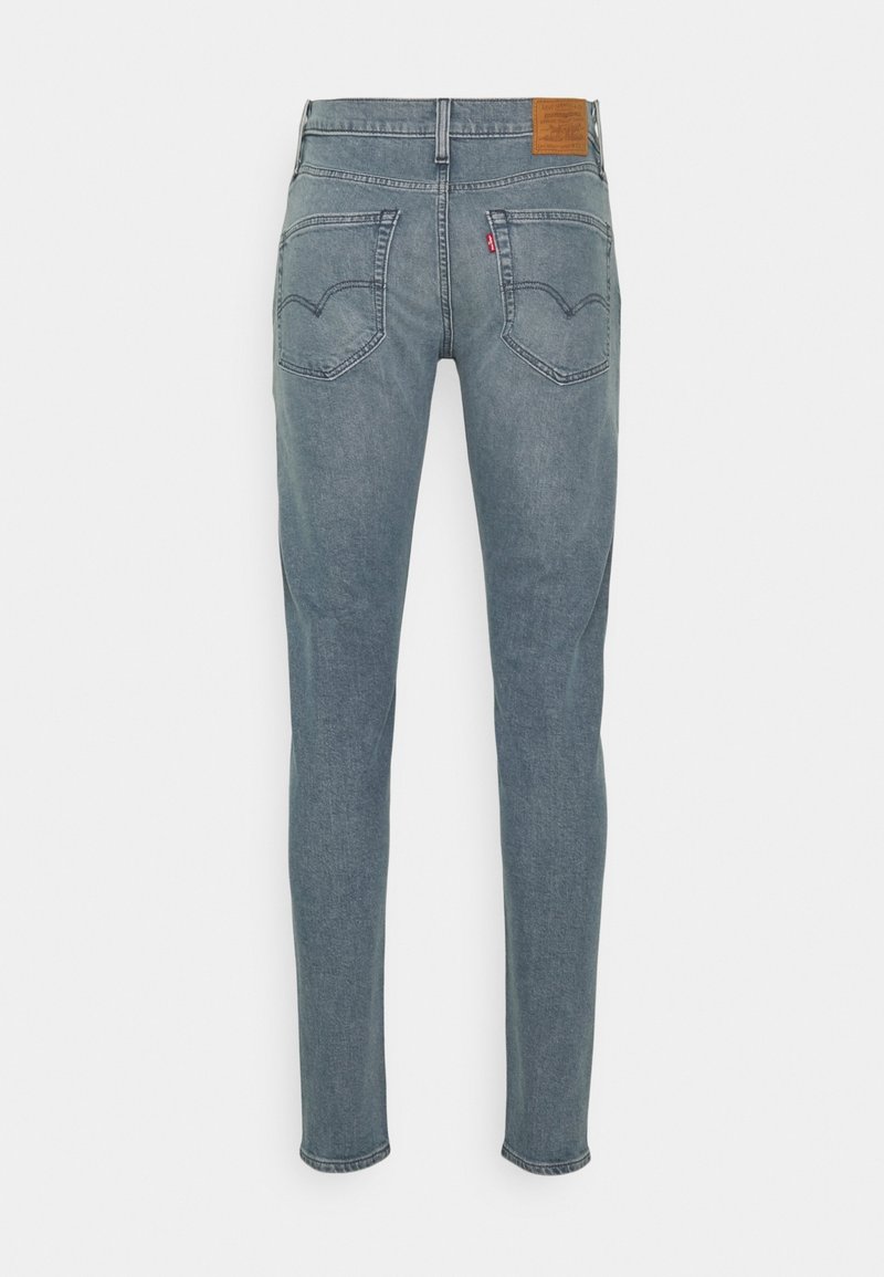 Jeans de mezclilla azul claro con piernas estrechas, que cuentan con dos bolsillos traseros y una etiqueta de cuero marrón en la cinturilla con detalle de costura.