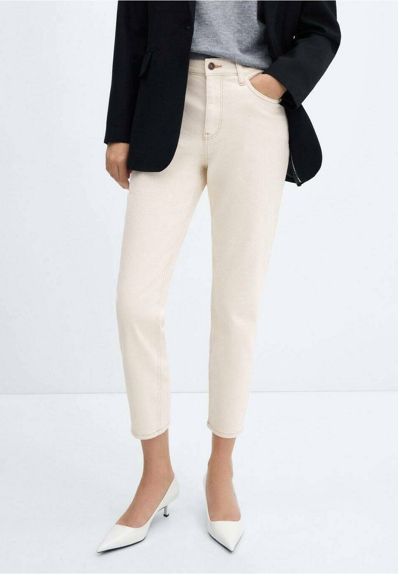 Jeans beige chiaro con una vestibilità su misura, caratterizzati da vita alta, cuciture minime e una lunghezza leggermente cropped, abbinati a un blazer nero.