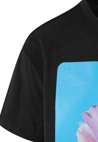 Črna bombažna majica s kvadratnim grafičnim potiskom na svetlo modrih toni in abstraktnim cvetličnim dizajnom v rožnatih in belih odtenkih.