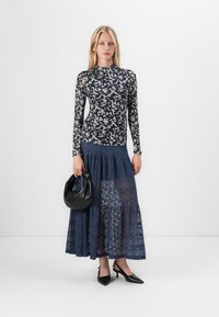 Long-sleeve top with black and white abstract pattern, paired with a navy tiered lace maxi skirt. Model holds a black round handbag.